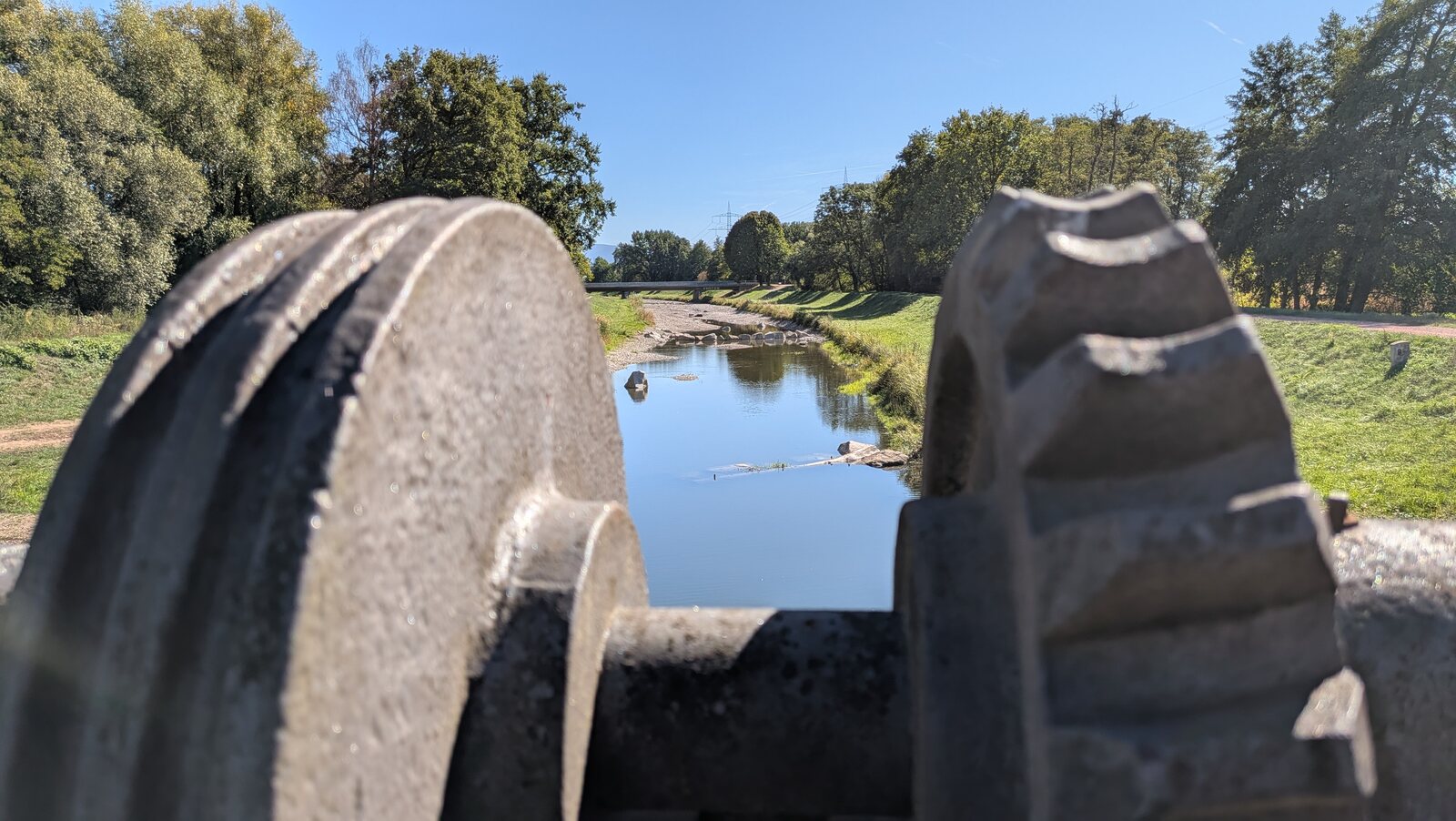 Wasserlauf von einer Brücke aus gesehen, mit Metallteilen im Vordergrund.